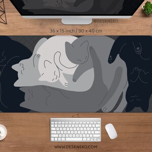 May include: A rectangular desk mat featuring a design of stylized cats in shades of gray and black. The mat measures 36 x 15 inches. The text "@DESKNEKO" and "WWW.DESKNEKO.COM" are printed on the mat.