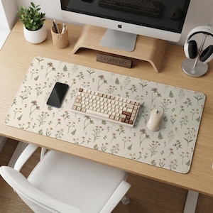 May include: A beige desk mat with a floral pattern, a matching keyboard and mouse, and a black smartphone. The desk is made of light wood. A small plant in a white pot is on the desk.