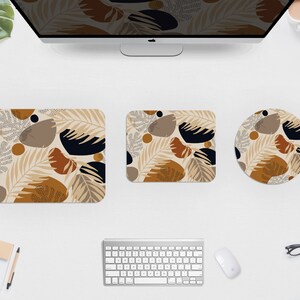 May include: A computer desk setup featuring a monitor, keyboard, mouse, and three matching desk accessories. The accessories include a square coaster, a rectangular mousepad, and a round mousepad. Each item has a beige background with a repeating pattern of brown, black, and tan shapes.