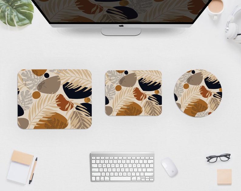 May include: A computer desk setup featuring a monitor, keyboard, mouse, and three matching desk accessories. The accessories include a square coaster, a rectangular mousepad, and a round mousepad. Each item has a beige background with a repeating pattern of brown, black, and tan shapes.
