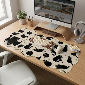 May include: A beige desk mat with a black cat pattern, a keyboard, mouse, and a smartphone. The mat has a unique cloud shape. A computer monitor and a cup of coffee are also on the desk.