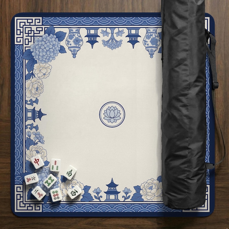May include: A blue and white Mahjong game mat with floral and pagoda designs. The mat has a cream-colored center with a lotus flower emblem. A black carrying case is visible on the right side. Several Mahjong tiles are scattered on the mat.