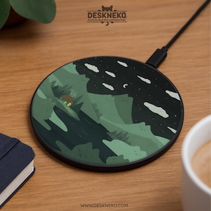 Puede incluir: Un cargador inalámbrico negro con un diseño de montaña y cielo nocturno. El cargador presenta un paisaje verde con una casa, nubes y estrellas. El texto "Deskneko" y "www.deskneko.com" son visibles.