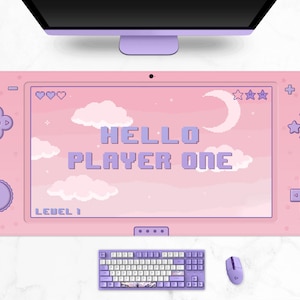 K&ouml;nnte beinhalten: Rosa Gaming-Mauspad mit Controller-Design. Das Mauspad zeigt den Text "HELLO PLAYER ONE" in pixeligen lila Buchstaben sowie Pixel-Art-Wolken, Sterne und einen Mond. Eine passende Tastatur und Maus sind ebenfalls sichtbar.