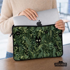 Puede incluir: Funda negra para portátil con un diseño de hojas verdes y caras de gatos negros ocultas. La funda tiene una cremallera y el logotipo de Deskneko. Diseñada para proteger un ordenador portátil.