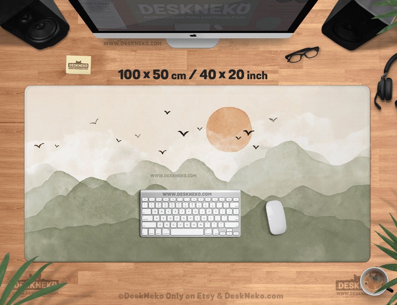 May include: A rectangular desk mat with a watercolor landscape design. The mat features a mountain range in shades of green and a setting sun. The dimensions are 40 x 20 inches. The text "DeskNeko" and "www.DESKNEKO.COM" are visible.