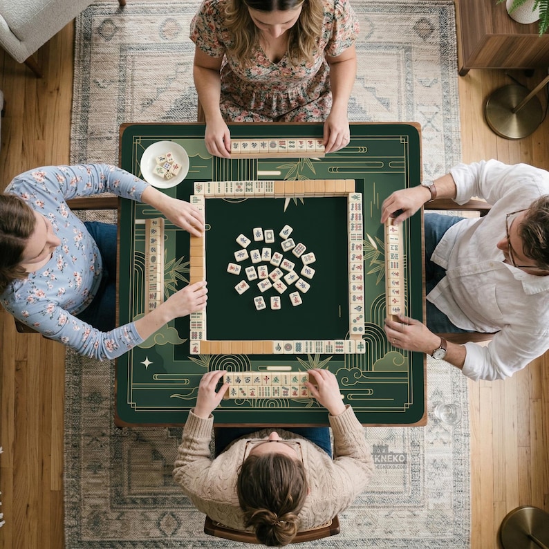 Pode incluir: Vista a&eacute;rea de um jogo de Mahjong. Quatro pessoas est&atilde;o sentadas em volta de uma mesa verde escura com detalhes dourados. As pe&ccedil;as de jogo bege est&atilde;o espalhadas sobre a mesa, que est&aacute; sobre um tapete estampado.