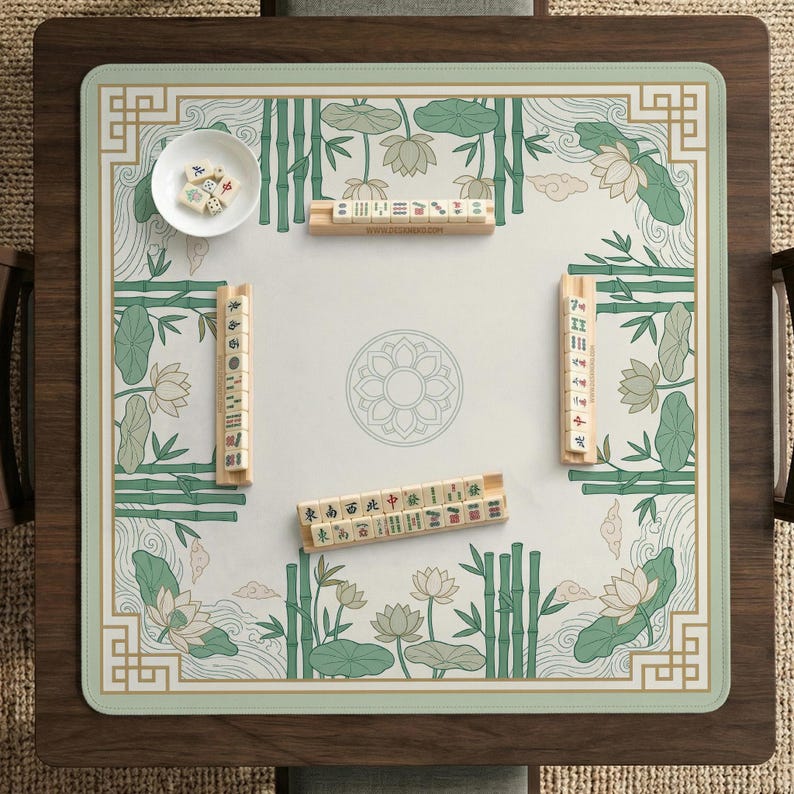 Puede incluir: Una mesa de juego de Mahjong cuadrada con un dise&ntilde;o floral verde y blanco, bamb&uacute; y flores de loto. La mesa tiene un marco de madera e incluye fichas y un cuenco peque&ntilde;o con dados. El juego est&aacute; listo para jugar.
