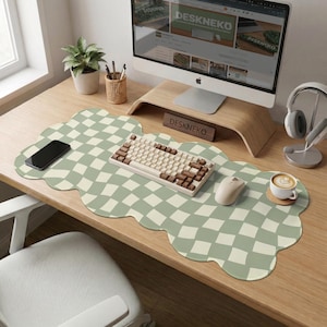 May include: A computer desk setup featuring a green and white checkered cloud-shaped desk mat. A keyboard, mouse, and smartphone are on the mat. A computer monitor, headphones, and a coffee cup are also visible. The desk has a wooden finish.