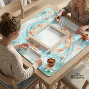 K&ouml;nnte beinhalten: Eine quadratische Mahjong-Matte mit einem hellblauen und wei&szlig;en Aquarell-Design mit orangefarbenen Koi-Karpfen und Lotusblumen. Die Matte zeigt eine zentrale quadratische Anordnung von Mahjong-Steinen sowie weitere Steine in den H&auml;nden der Spieler.