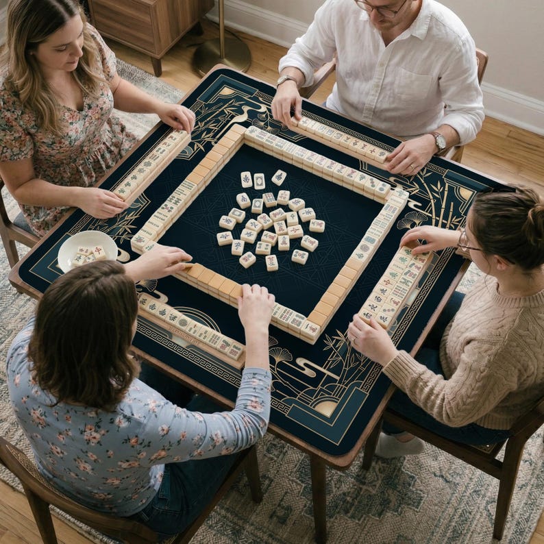 以下が含まれることがあります： 麻雀をしている人々のグループ。ゲームは、金のアクセントが付いた濃い青色のテーブルにセットされています。麻雀牌はベージュ色で黒いシンボルが付いています。プレイヤーはテーブルの周りに座っており、それぞれが牌のラックを持っています。