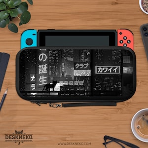 May include: A black and white Switch case with a cityscape design and Japanese text, including the word "KAWAII", and a cat silhouette. The case is on a wooden surface with a Switch console, a phone, and a coffee cup. The website address is visible.