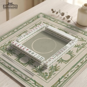 May include: A Mahjong set displayed on a beige mat with green bamboo patterns. The white tiles feature black and red characters and symbols. The mat has a central playing area.