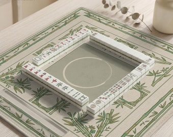May include: A complete Mahjong set arranged on a bamboo-themed mat. The tiles are white with black and red markings. The mat is beige with green bamboo illustrations and a central playing area.
