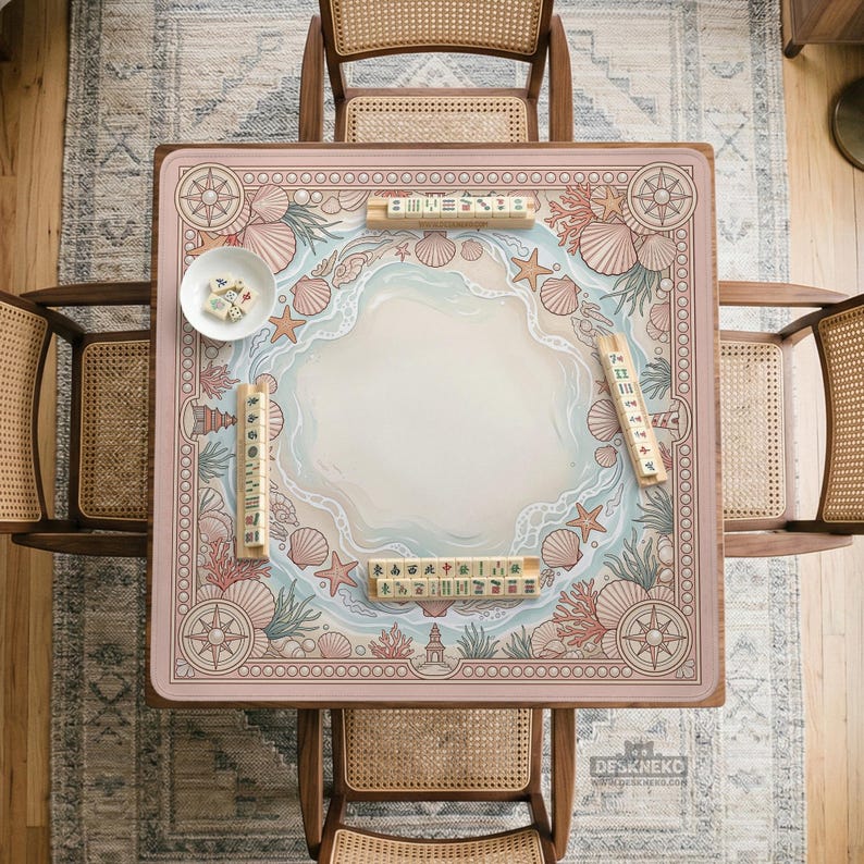 May include: A square Mahjong table with a pink border featuring a nautical design with seashells, starfish, and a lighthouse. The center has a light blue and white wave pattern. Wooden chairs surround the table, and Mahjong tiles are placed on the table.