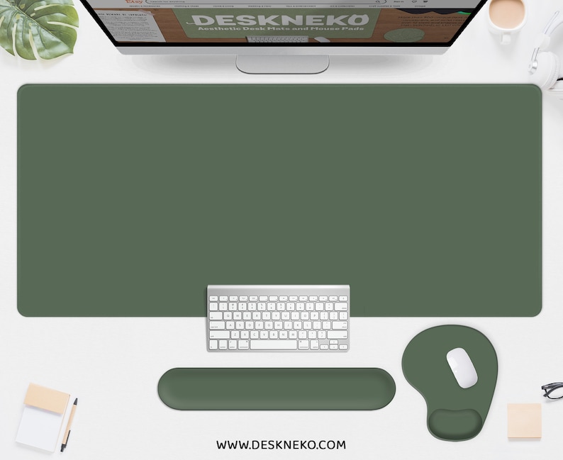 May include: A desk setup featuring a large olive green desk mat, a white keyboard, a matching wrist rest, and a mousepad with a white mouse. The website DESKNEKO is displayed on the monitor. The website address www.deskneko.com is visible at the bottom.