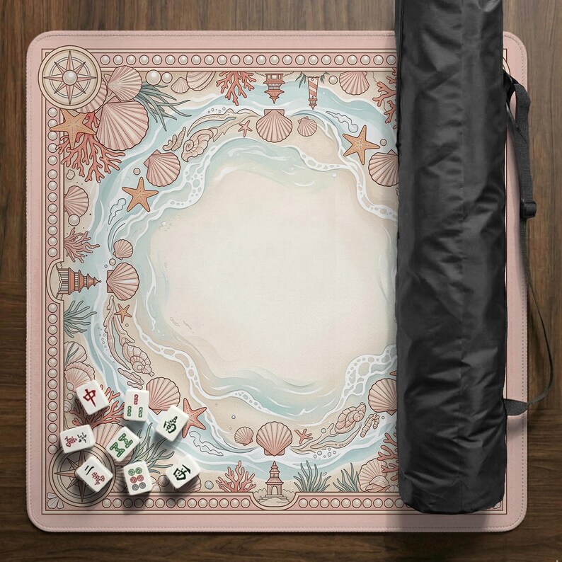 May include: A pink Mahjong mat with a beach-themed design featuring seashells, starfish, and a lighthouse. The mat has a border with a compass rose and a black carrying case is next to it. Several Mahjong tiles are scattered on the mat.