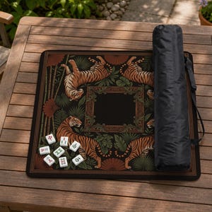 May include: A black mahjong mat with a tiger design, bamboo, and decorative frame. The mat has a black carrying case and several white mahjong tiles. The tigers are orange and black.