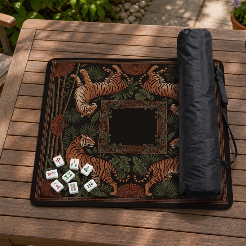 May include: A black mahjong mat with a tiger design, bamboo, and decorative frame. The mat has a black carrying case and several white mahjong tiles. The tigers are orange and black.