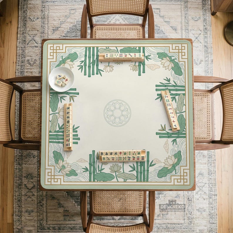 Puede incluir: Vista a&eacute;rea de una mesa de Mahjong cuadrada con una superficie crema, adornada con bamb&uacute; verde, flores de loto y bordes decorativos. La mesa est&aacute; rodeada por cuatro sillas de madera con respaldos tejidos. Hay fichas de Mahjong y un cuenco peque&ntilde;o sobre la mesa.