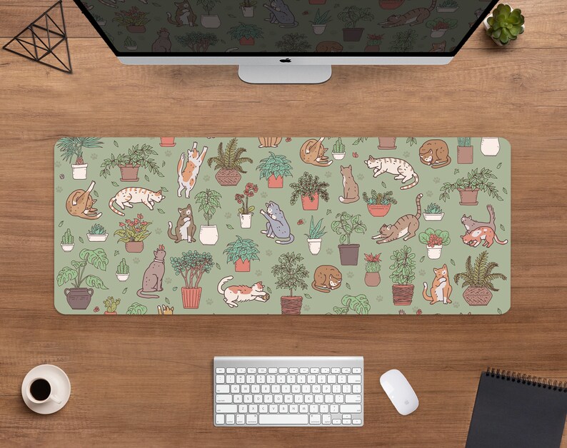 Puede incluir: Alfombrilla de escritorio rectangular con un patr&oacute;n repetido de gatos de dibujos animados y plantas en macetas sobre un fondo verde salvia. Los gatos est&aacute;n en varias poses, y las plantas est&aacute;n en macetas de terracota. Se ve una computadora, un teclado y un rat&oacute;n.