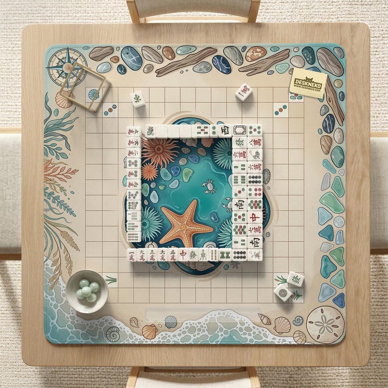 May include: A square wooden mahjong table with a beach-themed design. The center features a turquoise ocean scene with a starfish and coral. The border has seashells, pebbles, and the text "DESKNEKO". Mahjong tiles and dice are arranged on the table.