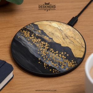 Puede incluir: Cargador inalámbrico redondo negro con un diseño abstracto dorado y negro. El cargador tiene un borde y un cable negros. El diseño incluye puntos dorados y un patrón similar a una montaña. La marca "Deskneko" es visible.