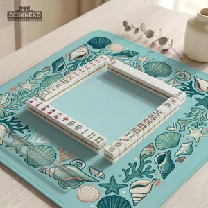 May include: A Mahjong set with white tiles and Chinese characters is arranged on a light blue mat. The mat features a sea-themed design with seashells, starfish, and coral. The game is set on a light wooden surface.