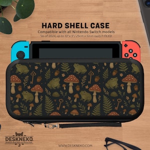 May include: Black hard shell case for Nintendo Switch, adorned with a pattern of green frogs, red mushrooms, keys, and ferns. Compatible with all Nintendo Switch models, it measures up to 25cm x 12cm. The case has a wrist strap.