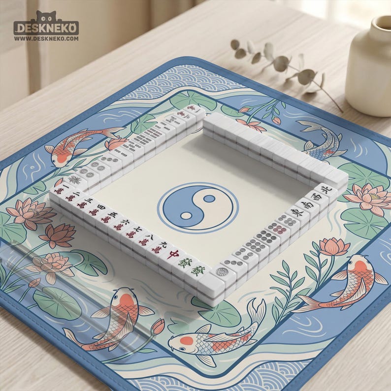 May include: A Mahjong set with white tiles and a Yin Yang symbol in the centre. The set is on a blue mat featuring koi carp and lotus flowers. The brand name "DESKNEKO" is visible. The mat's design is reminiscent of traditional Asian art.