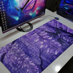 May include: A rectangular mousepad featuring a vibrant purple floral design, showcasing cascading wisteria blossoms. The pad is placed on a white desk, next to a computer monitor and a desktop computer.