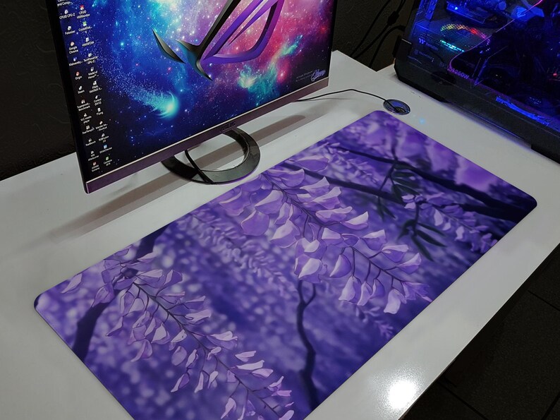 May include: A rectangular mousepad featuring a vibrant purple floral design, showcasing cascading wisteria blossoms. The pad is placed on a white desk, next to a computer monitor and a desktop computer.