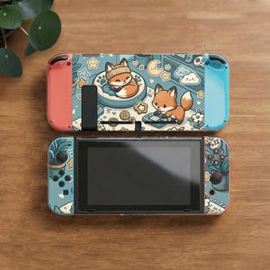 May include: A gaming console featuring a light blue skin with a repeating pattern of orange foxes, potted plants, stars, and clouds. The console has a black screen, a red left controller, and a light blue right controller with standard buttons.