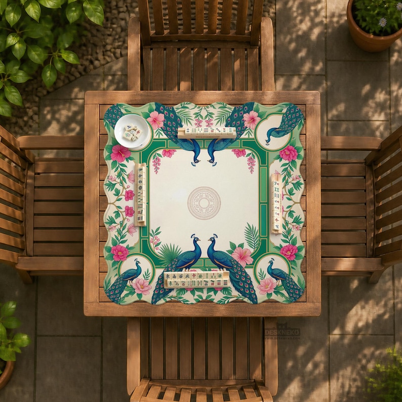May include: A square mahjong mat featuring a cream-colored center with a circular emblem, surrounded by a green border decorated with blue peacocks, pink hibiscus flowers, and green foliage. Four sets of mahjong tiles are placed on the mat.