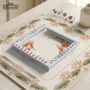 May include: A white Mahjong set arranged in a square on a cream-colored mat. The mat features a floral design with lotus flowers and koi fish. The tiles have red and green characters. The logo "DESKNEKO" is in the top left corner.