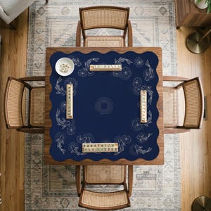 Puede incluir: Vista a&eacute;rea de una mesa de madera con un tapete azul marino con un dise&ntilde;o de peces koi y nen&uacute;fares. La mesa est&aacute; rodeada por cuatro sillas de rat&aacute;n. Hay fichas de mahjong y un plato blanco peque&ntilde;o sobre la mesa.