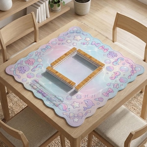 May include: A square, pastel-colored placemat with a scalloped edge, featuring sea creatures, bows, and bubbles. A wooden frame sits in the center. The placemat is on a wooden table with wooden chairs.