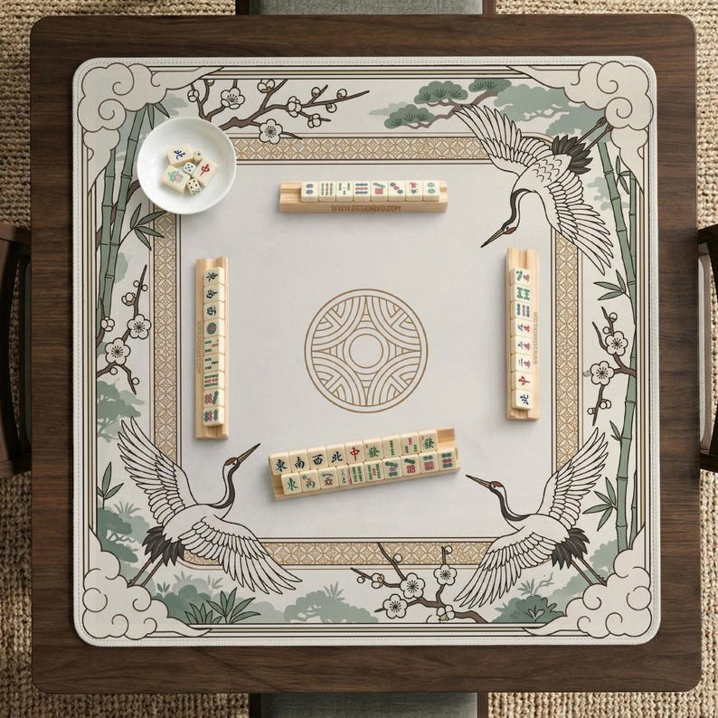 May include: Mahjong game set with a decorative playing surface featuring cranes, bamboo, and floral elements. The wooden game board has a square design with a central circular pattern. The set includes tiles and a small bowl.