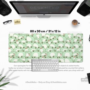 May include: A rectangular desk mat, 31 x 12 inches, featuring a repeating pattern of light green cartoon frogs on a pale green background. A white keyboard sits on the mat. The website address www.deskneko.com is visible.