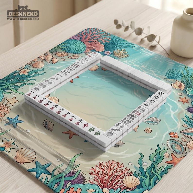 May include: A white Mahjong set arranged on a colorful mat with an ocean-themed design. The mat features illustrations of coral, seashells, and starfish. The game pieces are rectangular and display Chinese characters and symbols.