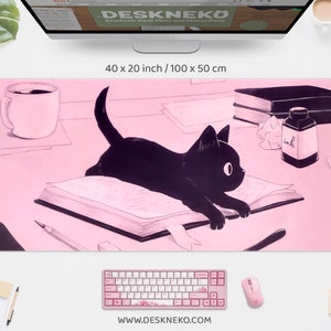 Könnte beinhalten: Ästhetische Schreibtischunterlage in Rosa mit einer Illustration einer schwarzen Katze. Die Matte misst 100 x 50 cm. Weitere Elemente sind eine Tastatur, eine Maus und eine Kaffeetasse. Die Website-Adresse ist unten sichtbar.