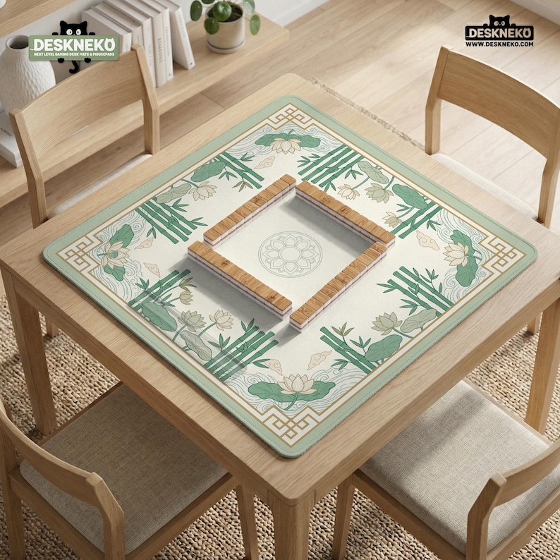 Puede incluir: Un tapete de juego cuadrado de color crema con un borde verde y un dise&ntilde;o floral y de bamb&uacute;. El tapete est&aacute; centrado en una mesa de madera, con piezas de juego de madera en el centro. El logotipo "DESKNEKO" es visible en las esquinas superiores.