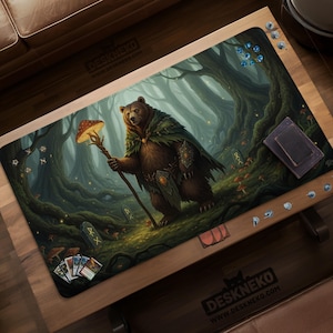 以下が含まれることがあります： 森の中にいる茶色のクマのキャラクターが描かれたゲームプレイマット。 クマはキノコの付いた杖を持ち、緑のマントを着ています。 マットにはカードスペース、サイコロエリア、テキスト「DESKNEKO」が含まれています。