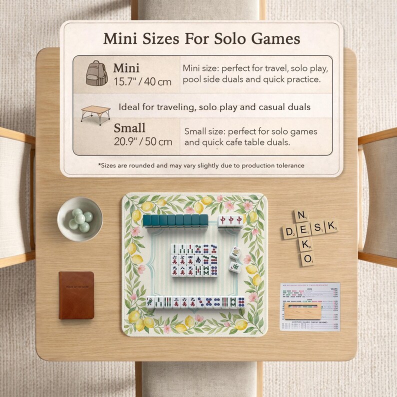 May include: A wooden table displays a mini Mahjong set with a floral and lemon-themed mat. The image includes a small brown notebook, a bowl of green spheres, and a sign that reads "Mini Sizes For Solo Games". The mini size is 15.7 inches / 40 cm.