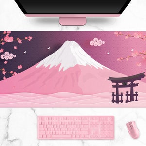 May include: A pink and white desk mat featuring a Japanese landscape with Mount Fuji, cherry blossoms, and a traditional torii gate. A pink keyboard, mouse, and headset are also visible.