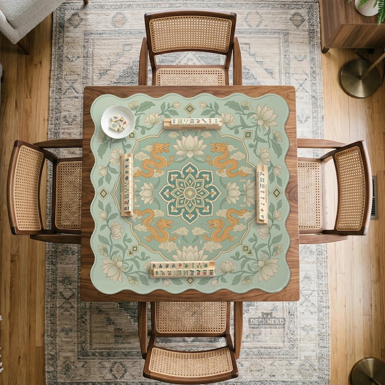 May include: A square wooden table with a scalloped-edge mat featuring a light green background, a central mandala, four golden dragons, and white lotus flowers. Four wooden mahjong tile racks are placed on the mat, along with a small white bowl.