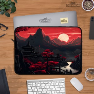 Puede incluir: Una funda negra para portátil con un diseño de paisaje japonés, con un cielo rojo, montañas y una luna llena. La funda tiene cierre de cremallera y el texto "DESKNEKO" es visible.