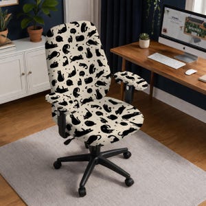 May include: An office chair with a black base and armrests. The chair's seat and back are covered in a cream-colored fabric patterned with black cat silhouettes in various poses. The chair is on a light gray rug.