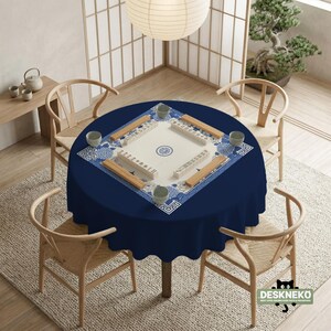 May include: A round, navy blue tablecloth covers a table set for a game. The table features a Mahjong set with tiles and wooden racks. Four light-colored chairs surround the table. The room has a Japanese-inspired aesthetic with a paper lantern and bonsai tree.