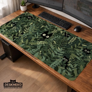 Peut inclure: Tapis de bureau rectangulaire vert et noir avec un motif de feuilles et des visages de chats noirs cachés. Le tapis porte l'inscription "WWW.DESKNEKO.COM". Idéal pour un clavier et une souris.